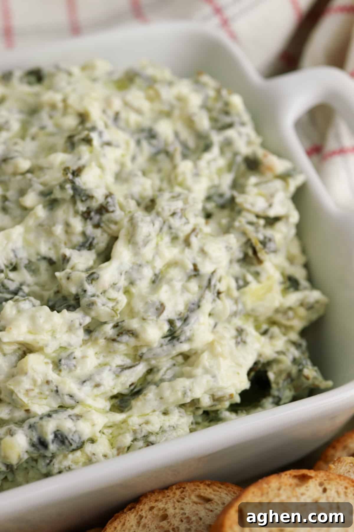 Creamy and cheesy slow cooker spinach artichoke dip in white serving bowl with small pieces of bread for dipping