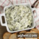 creamy crockpot spinach and artichoke dip in white bowl served with small pieces of bread for dipping