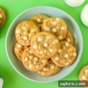 Banana pudding cookies with white chocolate chips on plate with glasses of milk and additional cookies in background.