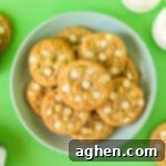 Banana pudding cookies with white chocolate chips on plate with glasses of milk and additional cookies in background.