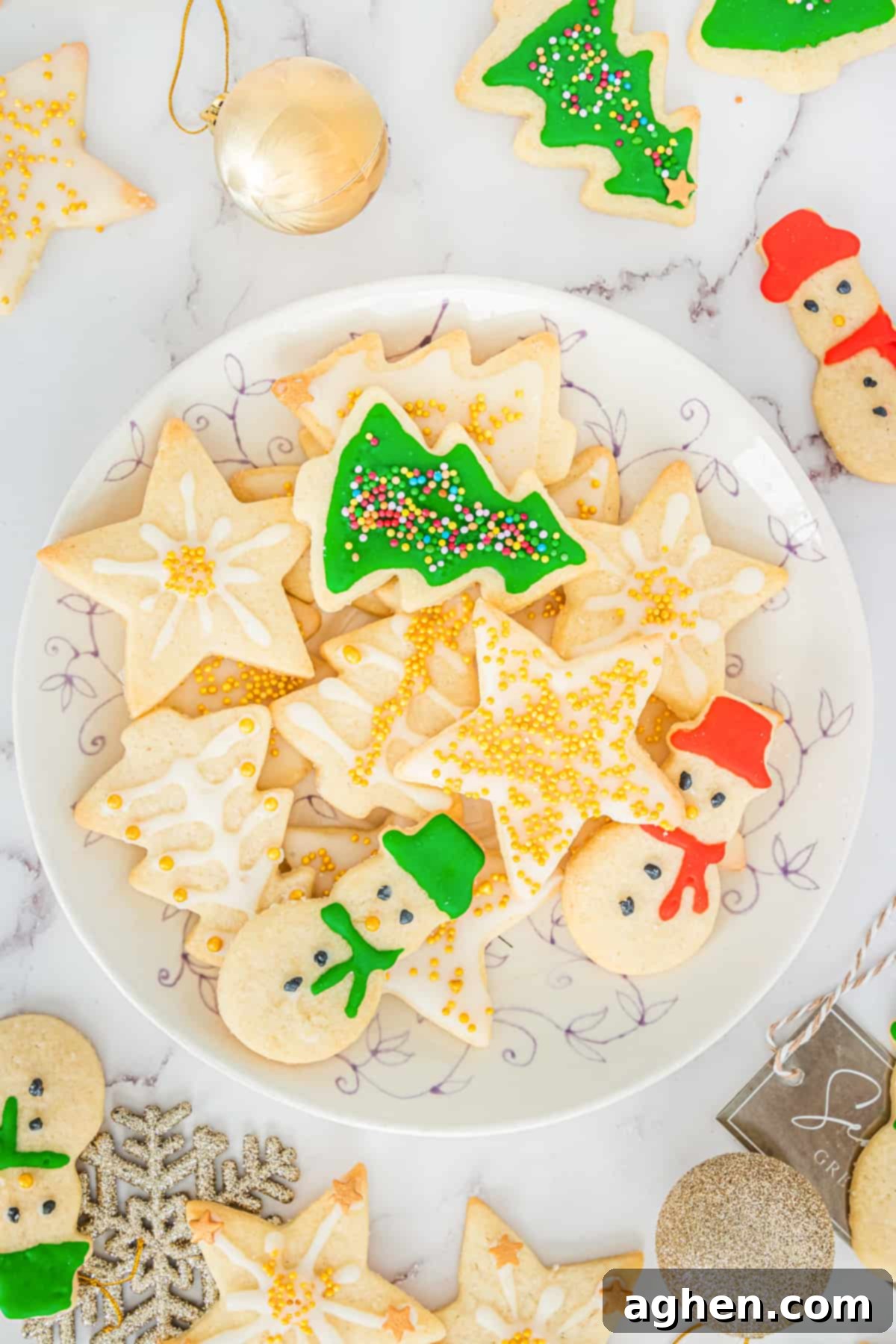 Decorated Christmas sugar cookies with icing and sprinkles on serving plate with additional cookies and Christmas ball ornaments scattered around table