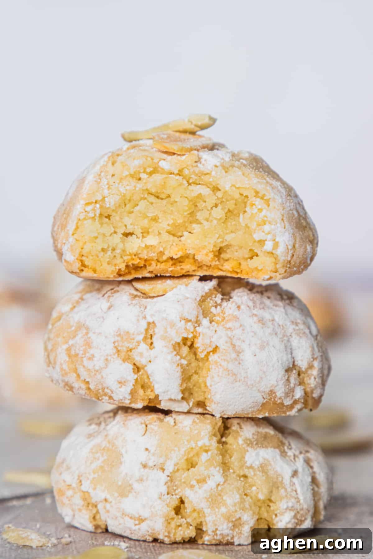 Three Italian Amaretti cookies on top of one another, with a top cookie broken in half to show soft, crumbly texture