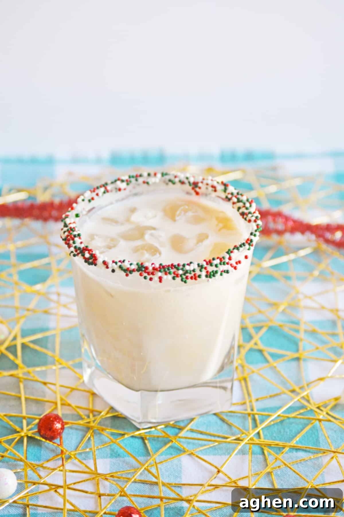 Christmas Cookie Cocktail with vodka in a christmas sprinkle rimmed glass, garnished with a mini sugar cookie