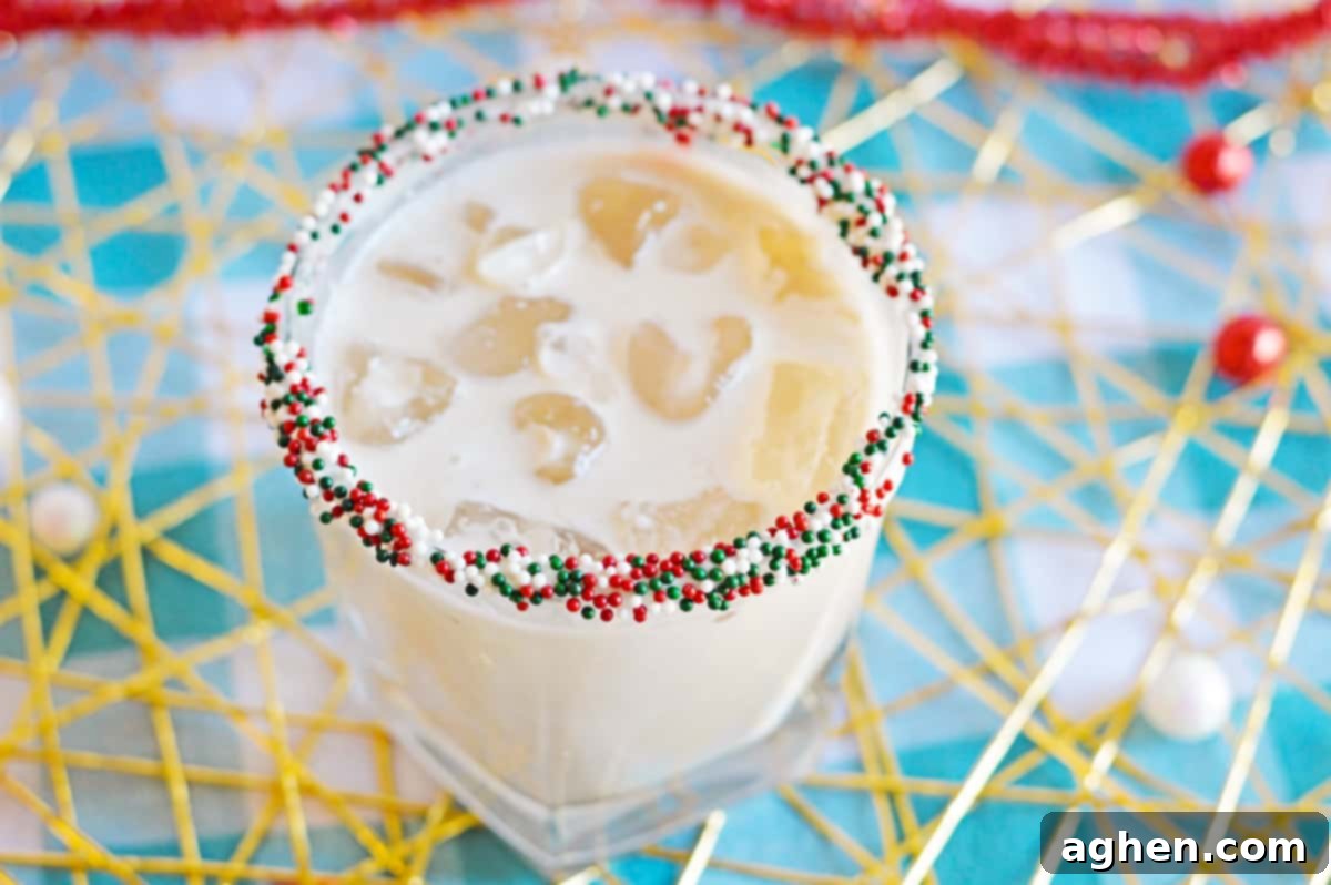White creamy cocktail in glass with ice and Christmas sprinkles on rim, ready to be enjoyed