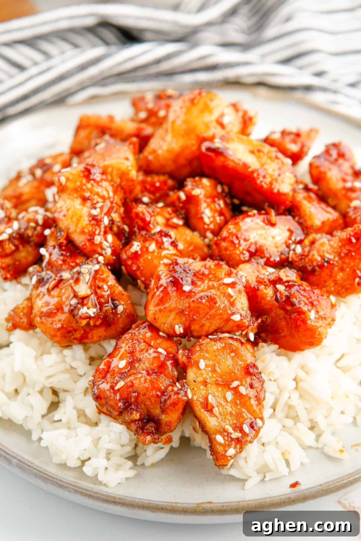 Honey sesame chicken breast pieces served over rice, garnished with fresh green onions and more sesame seeds.