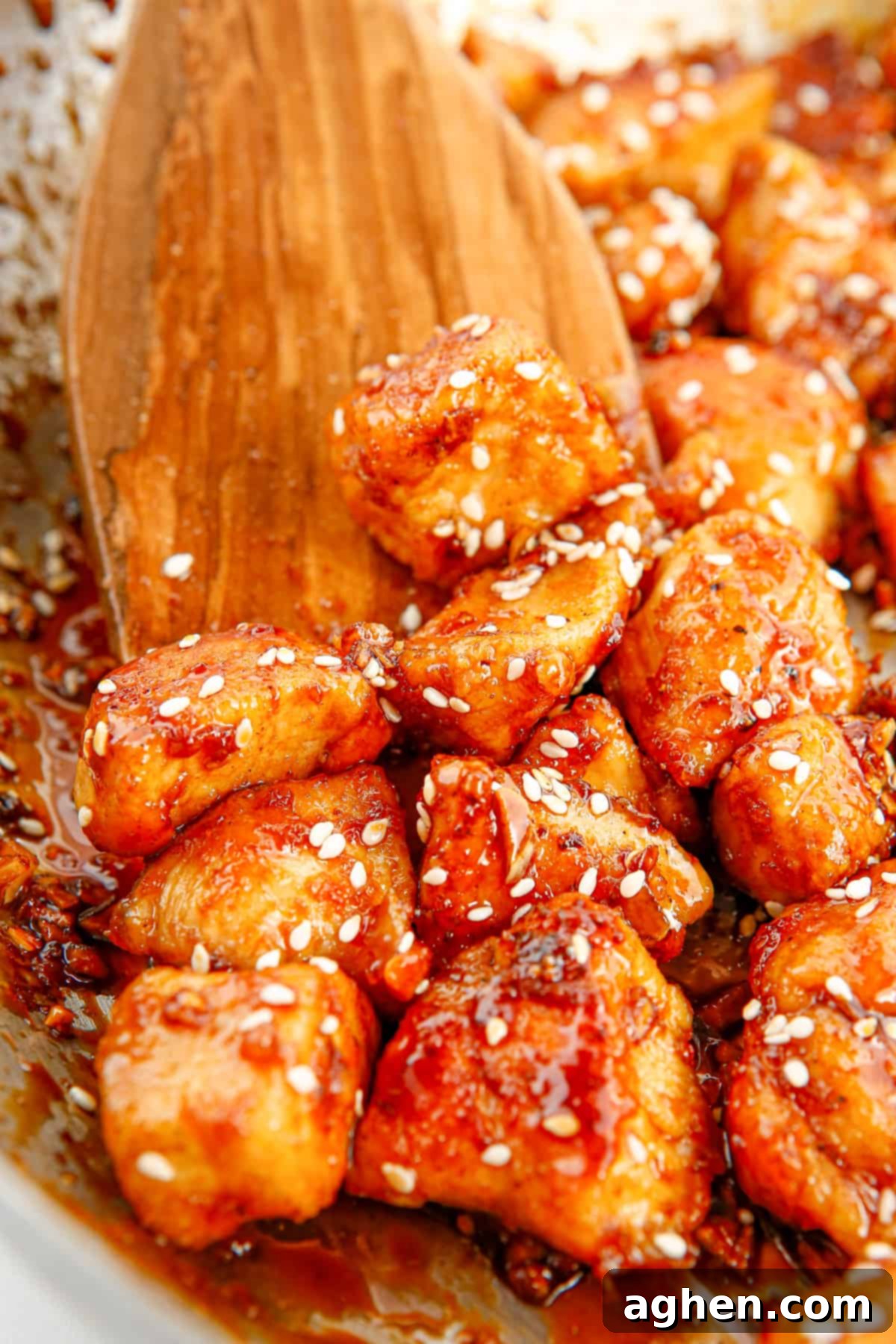 Wooden spoon stirring honey sesame chicken in a large non-stick skillet.