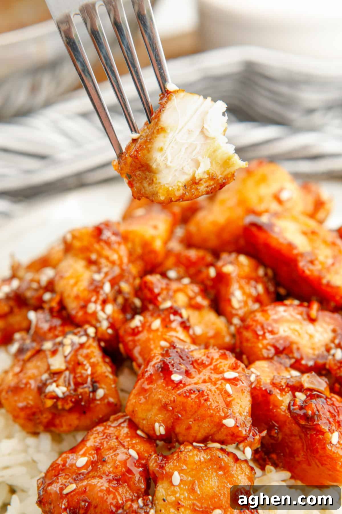 A piece of sesame garlic chicken on a fork with a bite taken out, showing the tender white chicken breast meat.