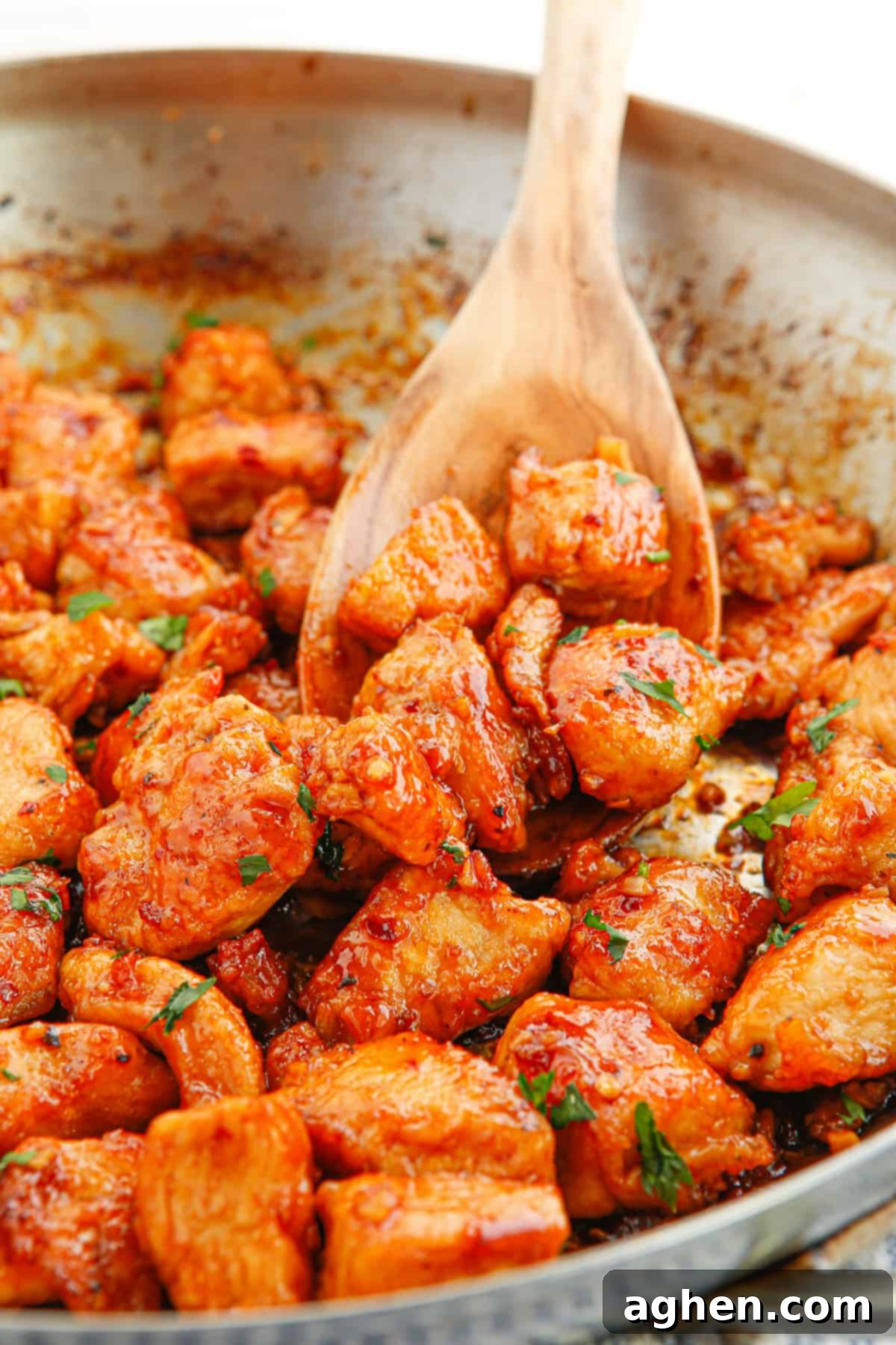 Pieces of spicy and sweet garlic chicken garnished with chopped parsley in a frying pan with wooden spoon