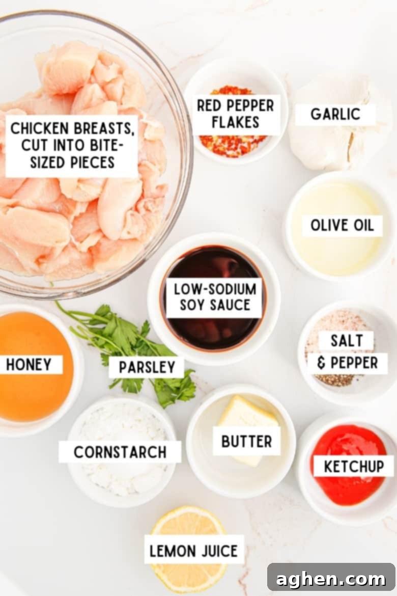 ingredients in bowls on countertop: chicken breasts cut into bite-sized pieces, red pepper flakes, olive oil, garlic, soy sauce, honey, cornstarch, butter, ketchup, lemon juice, salt and pepper, and parsley
