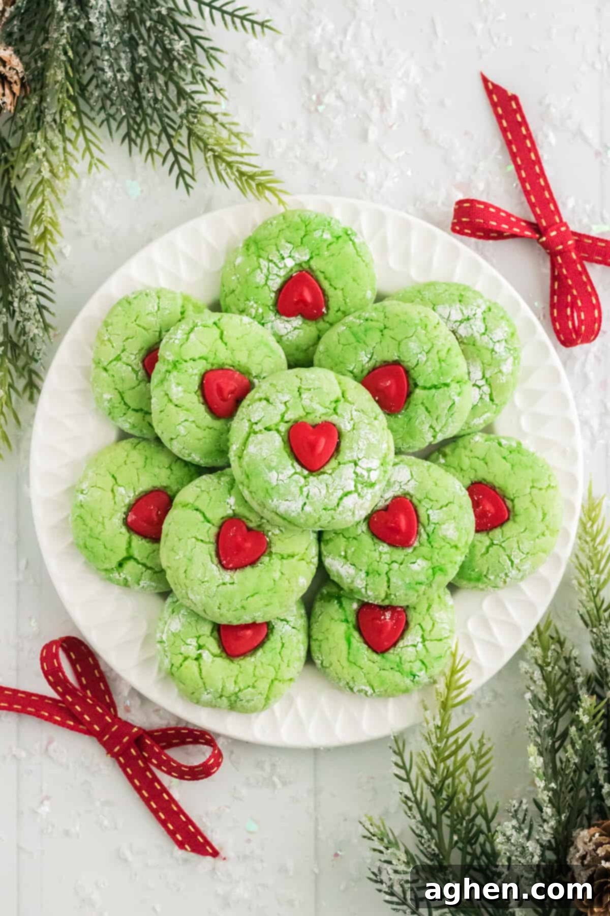 Festive Grinch Cookies 2 Grinch Cake Mix Cookies decorated with red heart candy in center on white serving plate with christmas decor around it