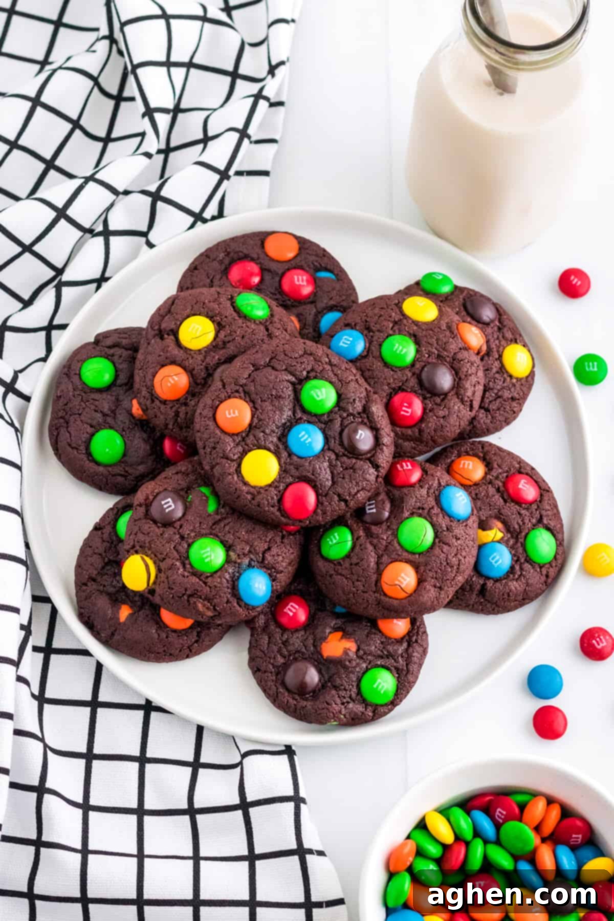 Easy M&M Chocolate Cake Mix Cookies 2 Chocolate cookies with M&Ms on white plate with glass of milk and more M&Ms next to them. A delicious snack.