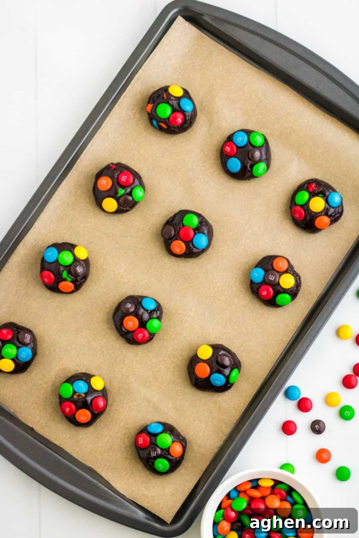 Easy M&M Chocolate Cake Mix Cookies 6 Balls of chocolate cake mix cookie dough with colorful M&Ms pressed into the top on a parchment lined baking sheet, ready for the oven.