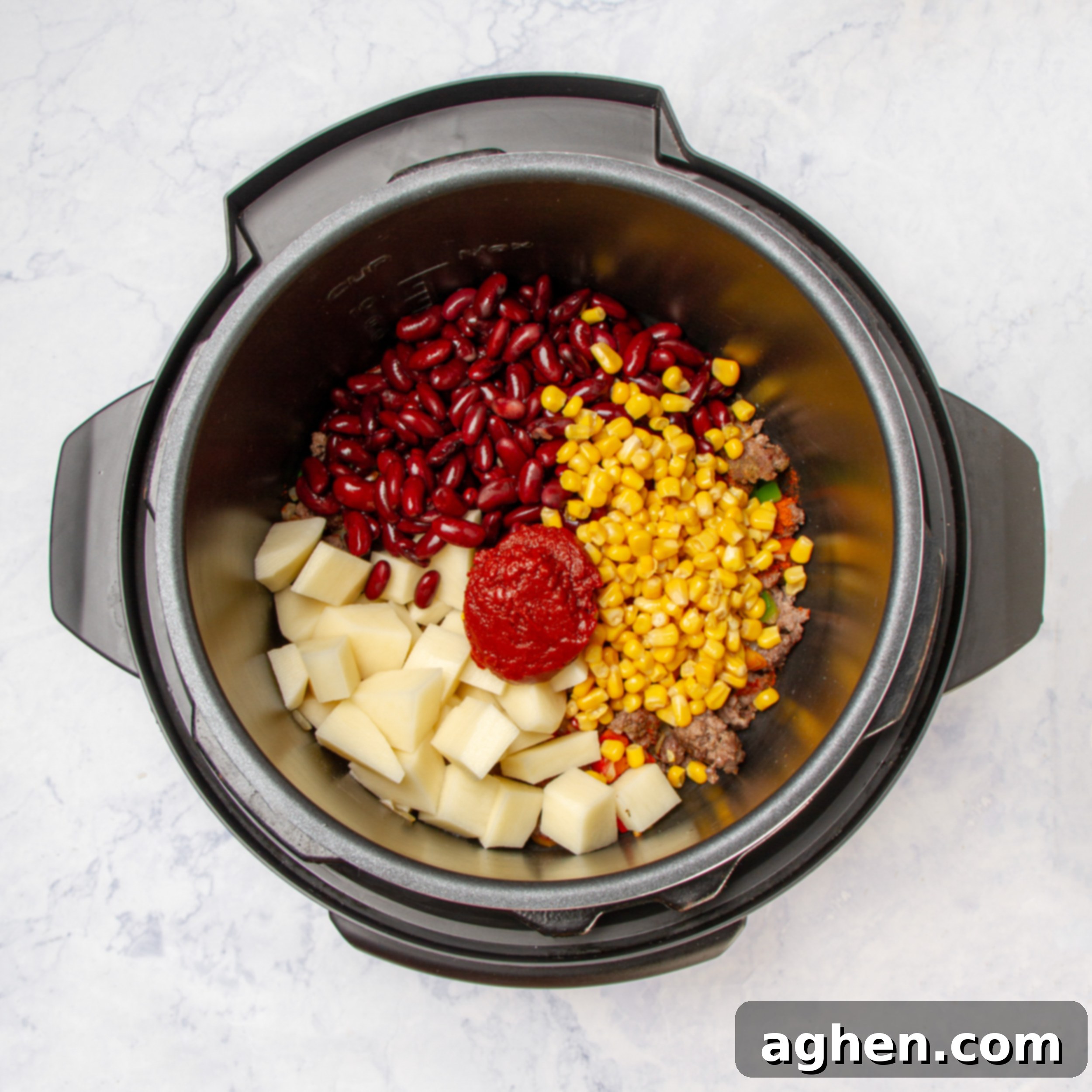 Chopped vegetables, red beans, and tomato paste added to the Instant Pot with sautéed ground beef, ready for mixing.