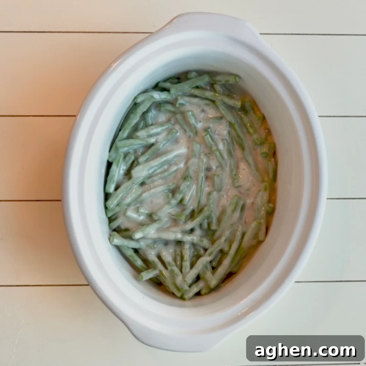 A slow cooker insert filled with a creamy green bean mixture, before the cooking process has begun, showcasing the fresh ingredients.