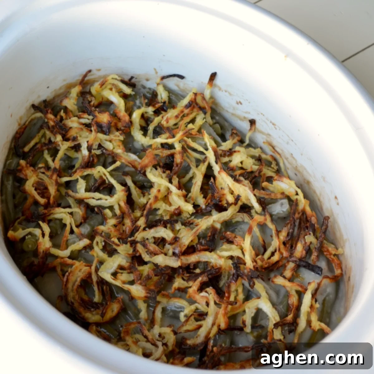 A close-up view of the finished slow cooker green bean casserole, topped with golden-brown crispy onions and steaming hot, ready to be served.