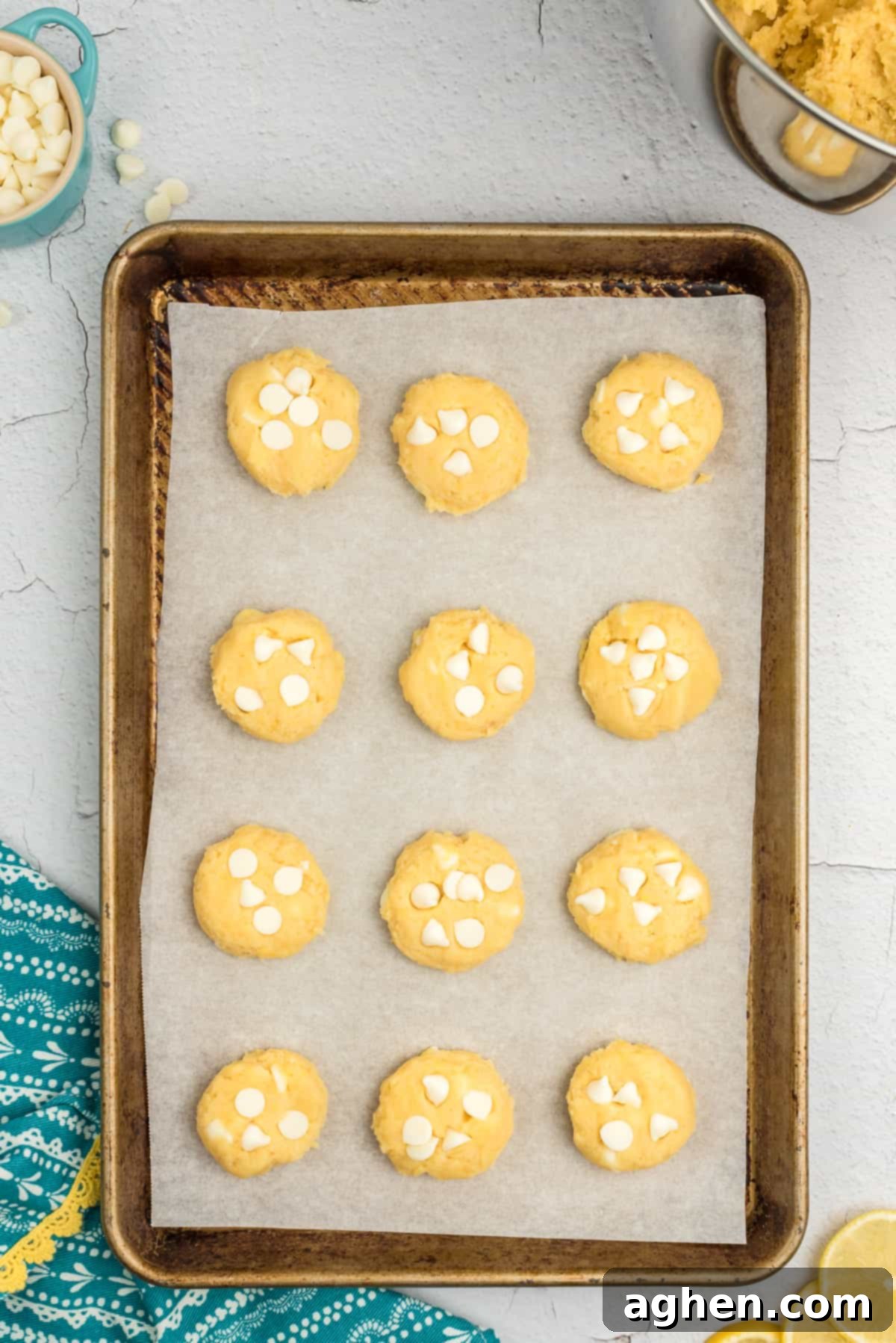 Lemon pudding mix cookie dough with white chocolate chips pressed into the tops, flattened slightly on a baking sheet.