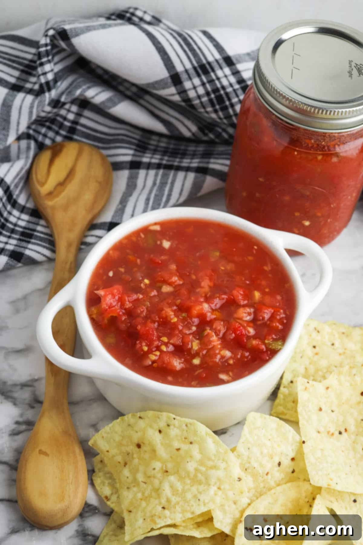 Bowl of homemade Rotel salsa with tortilla chips, cloth napkin, wooden spoons, and jar of homemade salsa in background