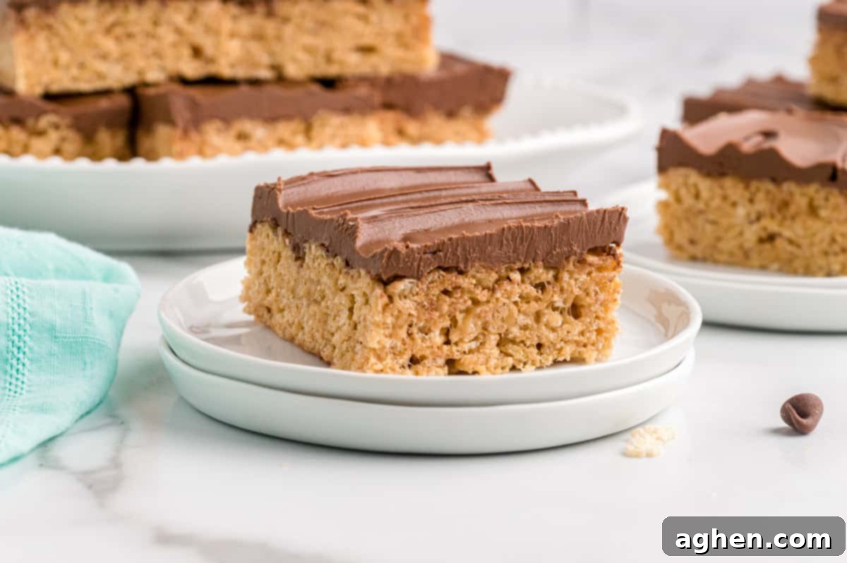 One chocolate topped peanut butter rice cereal treat on white plate with more treats in background.