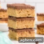 Peanut butter rice krispie treats with chocolate topping stacked on top of each other on white plate.