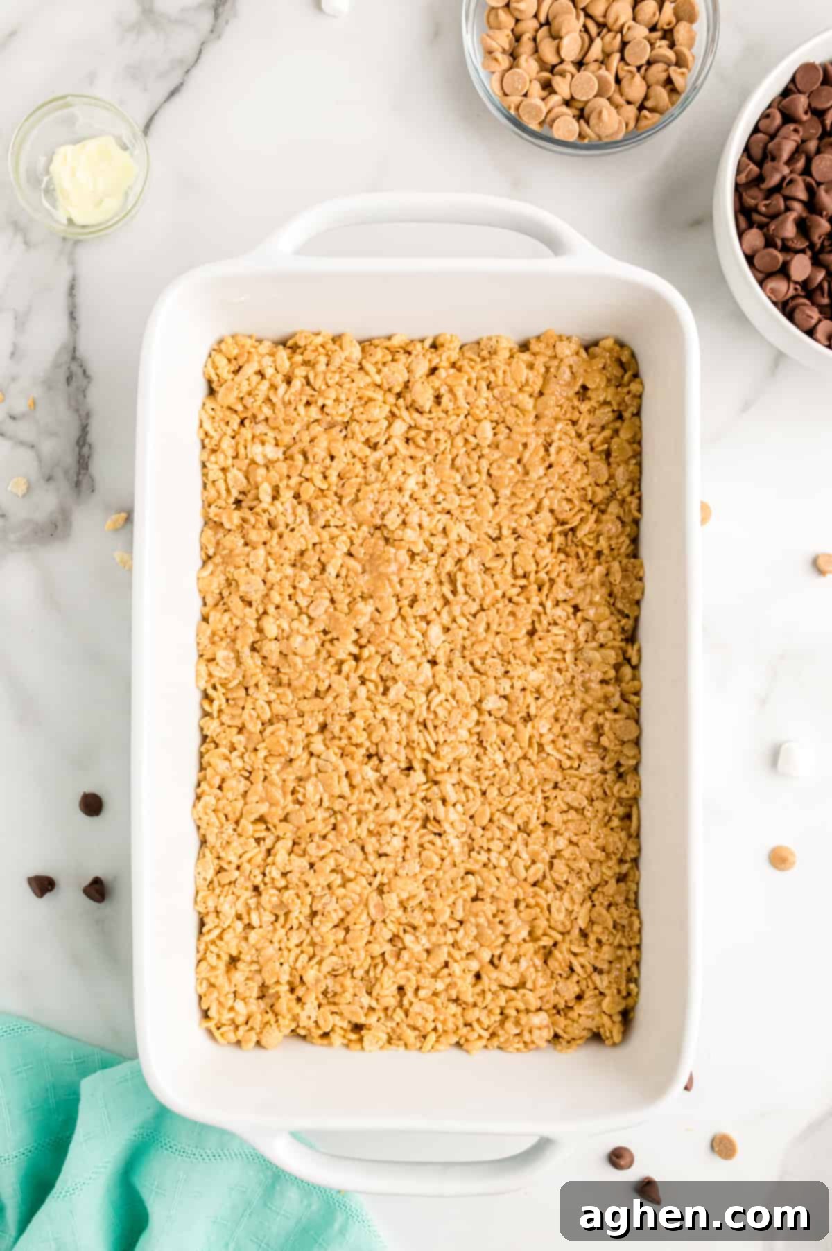 Peanut butter rice cereal mixture pressed into white 9 by 13 inch baking pan.
