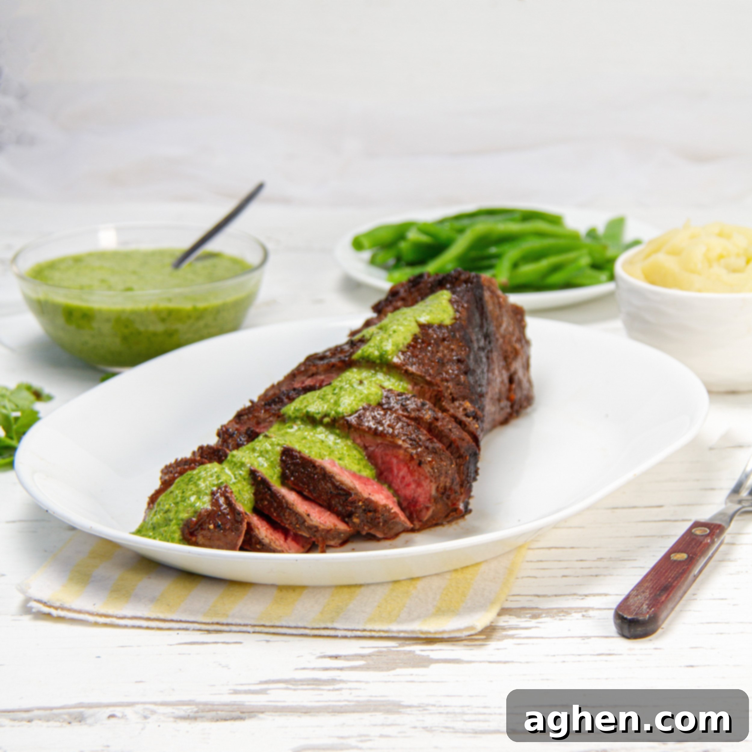 Juicy and tender London Broil sliced on a plate with green sauce drizzled on top.