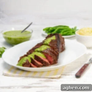 Juicy and tender London Broil sliced on a plate with green sauce drizzled on top.