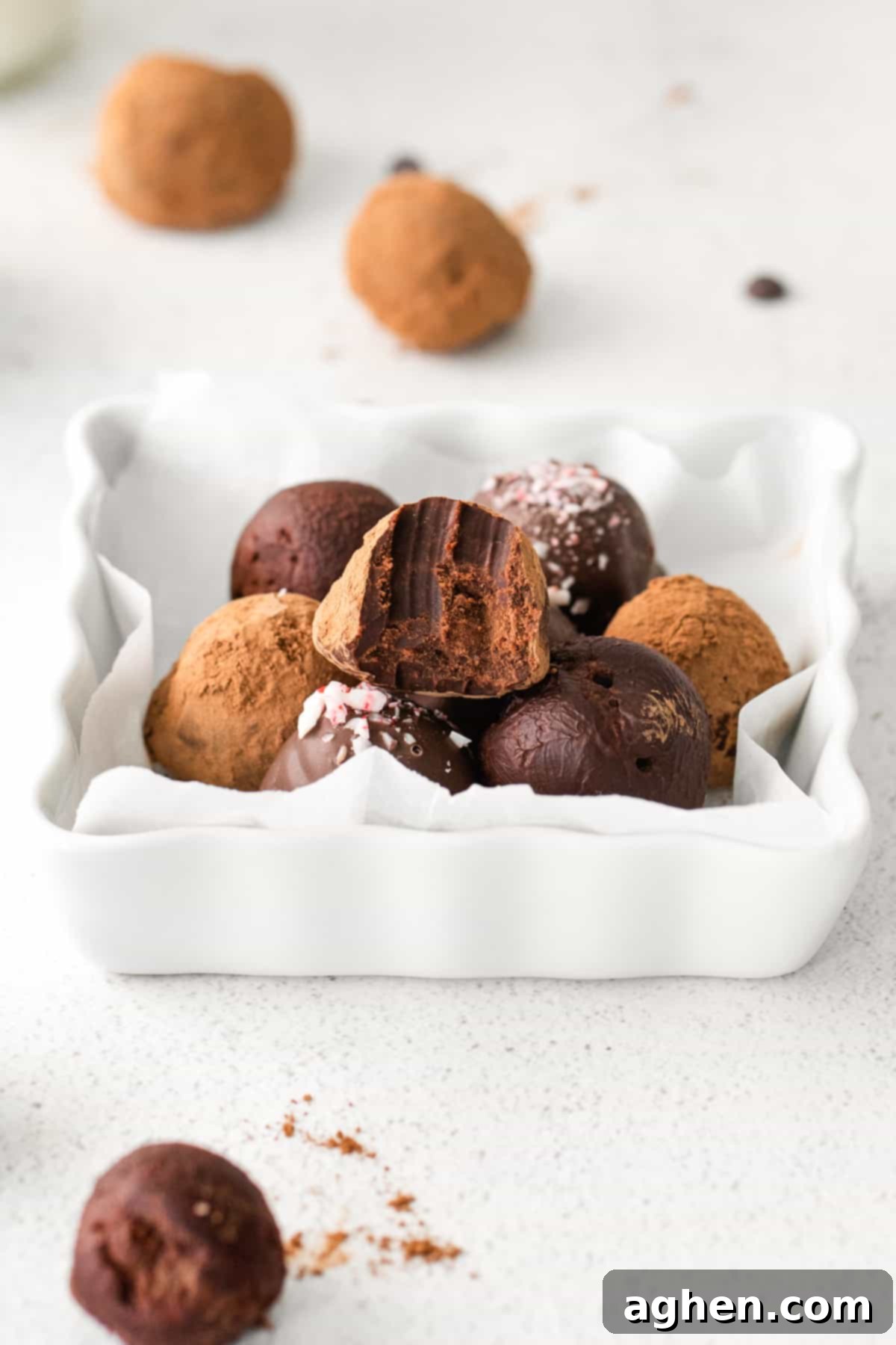 Boozy Dark Chocolate Peppermint Truffles on white plate, one truffle has a bite taken out of it to show rich and fudgey ganache center.