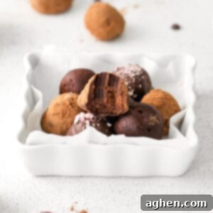 Boozy Dark Chocolate Peppermint Truffles on white plate, one truffle has a bite taken out of it to show rich and fudgey ganache center.