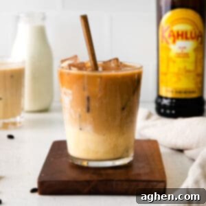 A glass of Eggnog White Russian cocktail with a spoon, accompanied by bottles of Kahlua and eggnog in the background.
