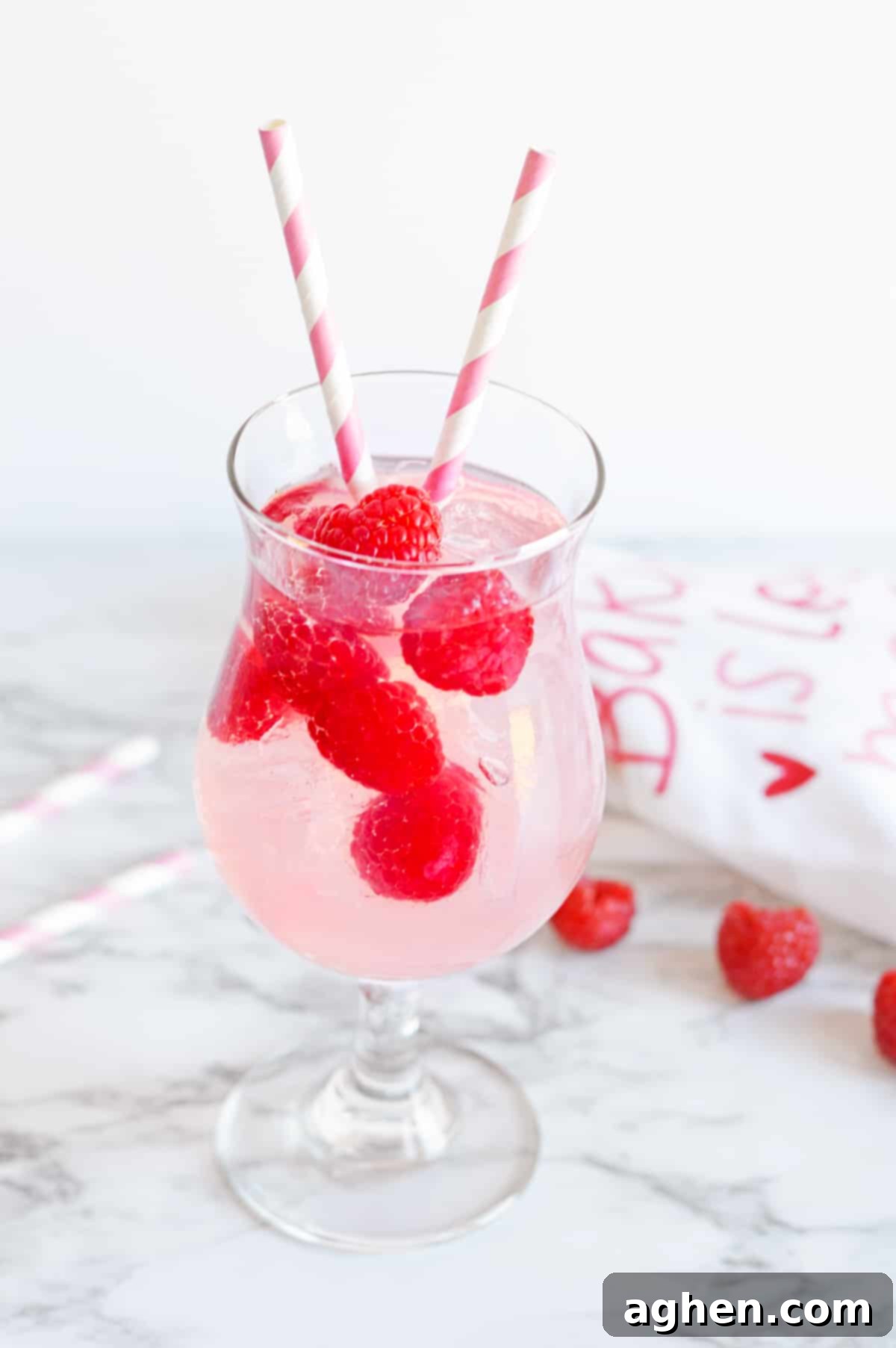 Pink Moscato Sangria with fresh raspberries in a cocktail glass with pink and white striped paper straws