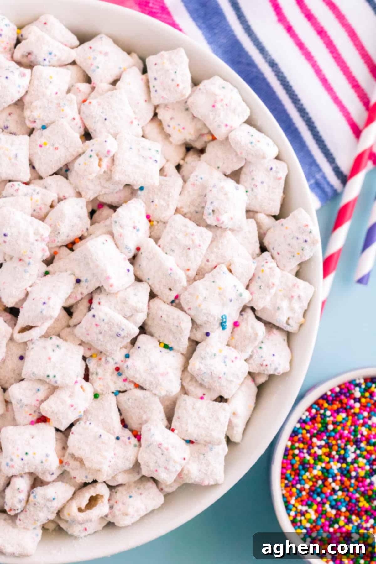 Top-down photo of funfetti chex mix muddy buddies in large white bowl with rainbow sprinkles in a smaller bowl beside them