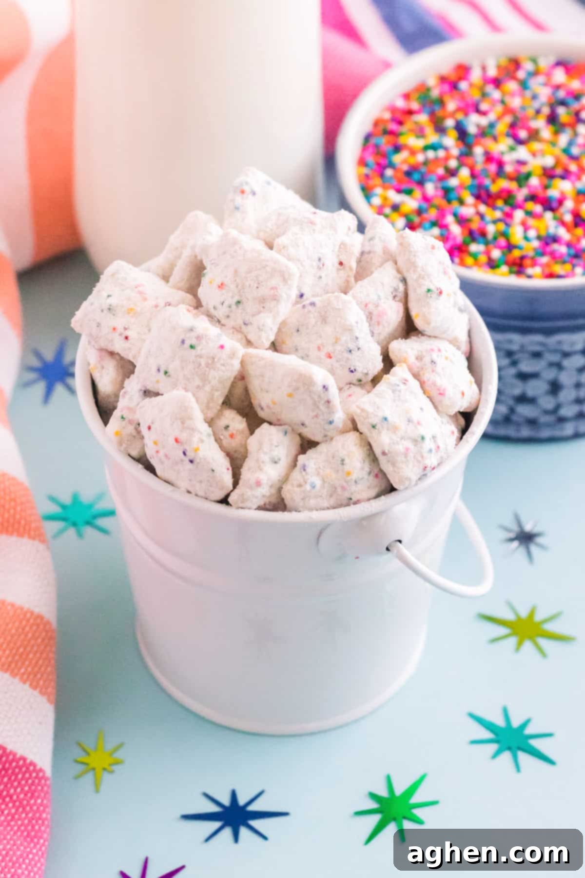 Birthday Cake Muddy Buddies in small silver pail with colorful sprinkles, confetti, and around it