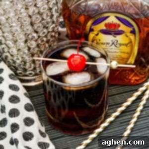 Whiskey Cherry Coke Cocktail in glass with ice cubes and maraschino cherry on skewer. Bottle of crown royal in background.