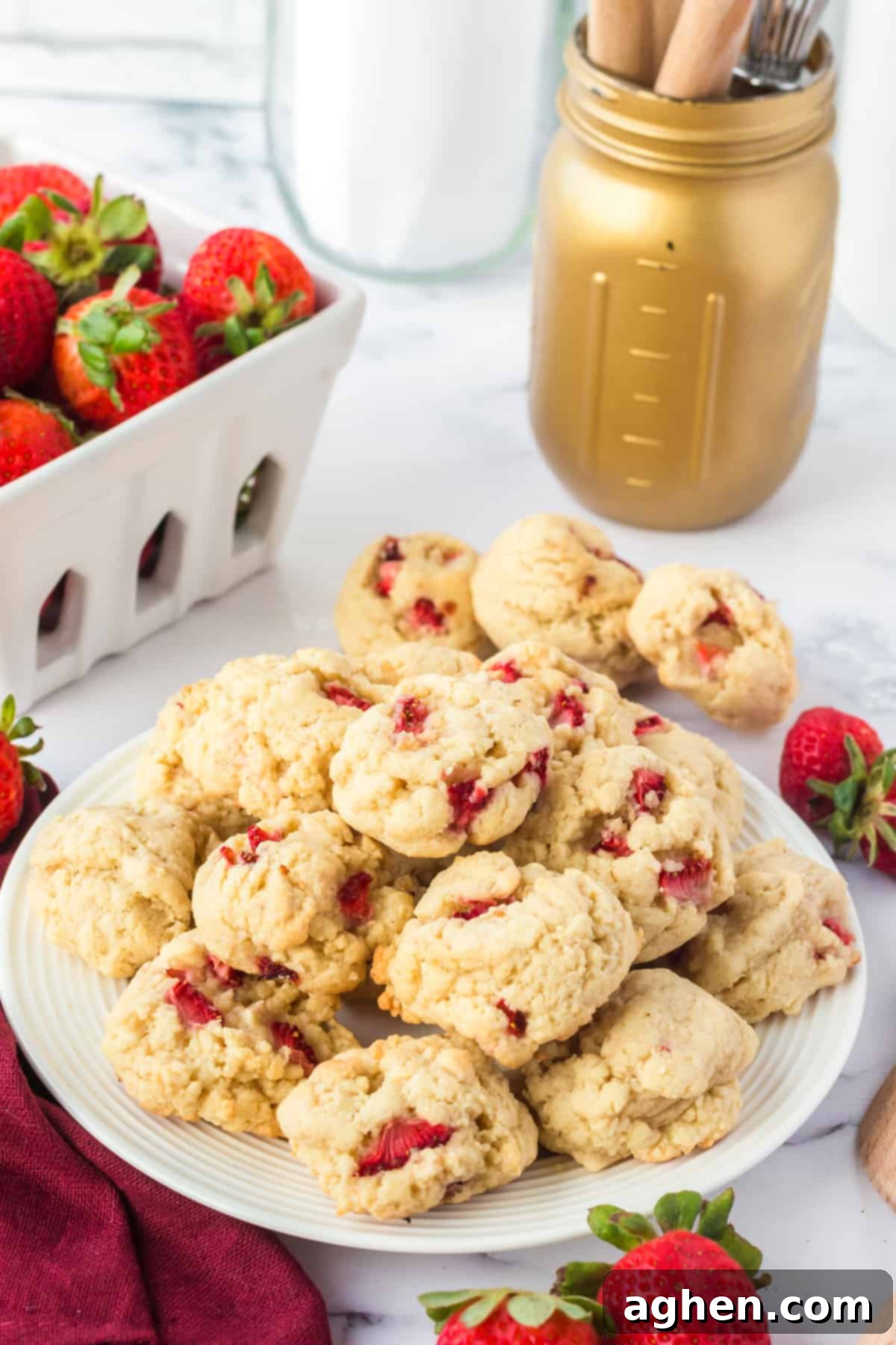 Delicious strawberry shortcake cookies arranged on a white plate, with a scattering of fresh, whole strawberries in the background, creating a vibrant and inviting scene.
