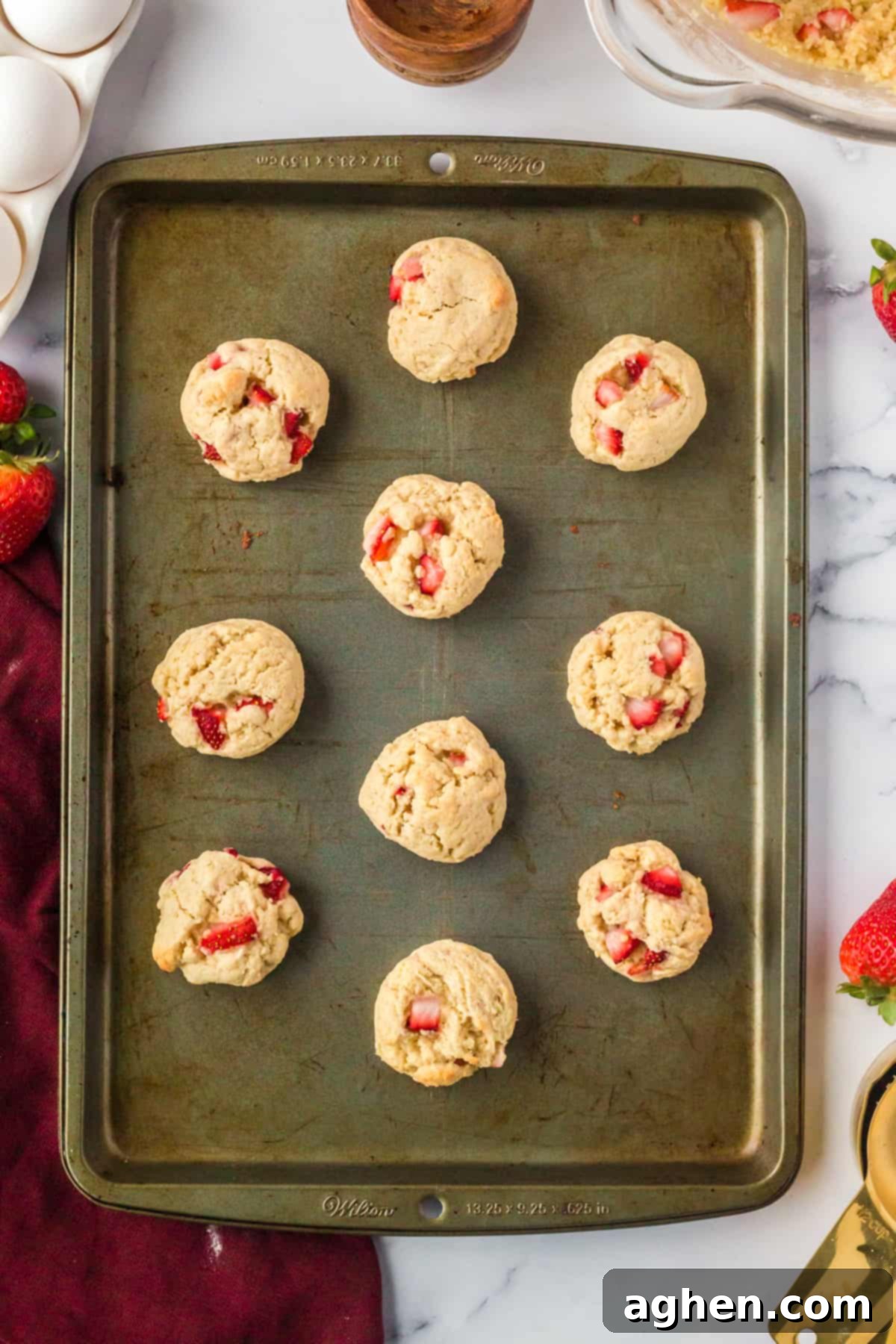Freshly baked strawberry shortcake cookies, golden around the edges and studded with vibrant red strawberries, cooling on a baking sheet after coming out of the oven.