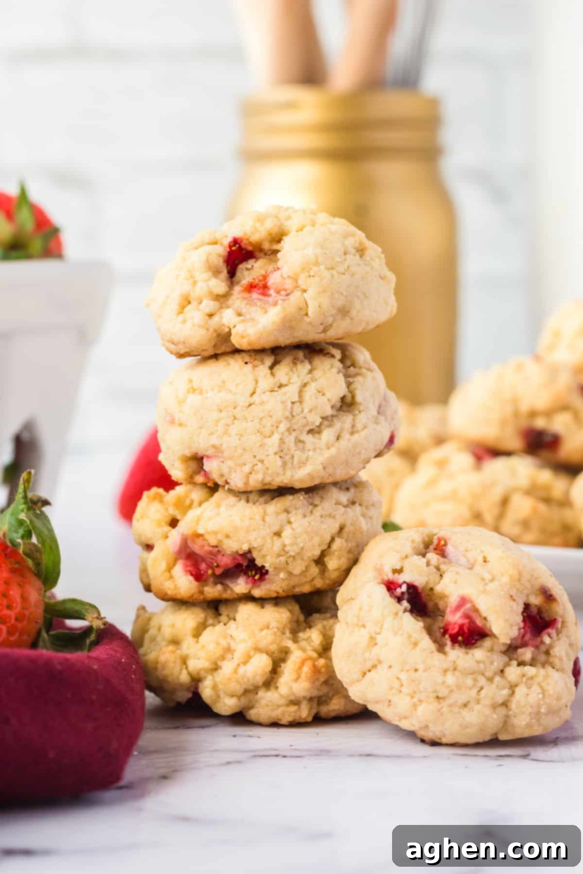 Four perfectly fluffy strawberry shortcake cookies stacked artfully, surrounded by more cookies and glistening fresh strawberries, highlighting their soft texture and vibrant color.
