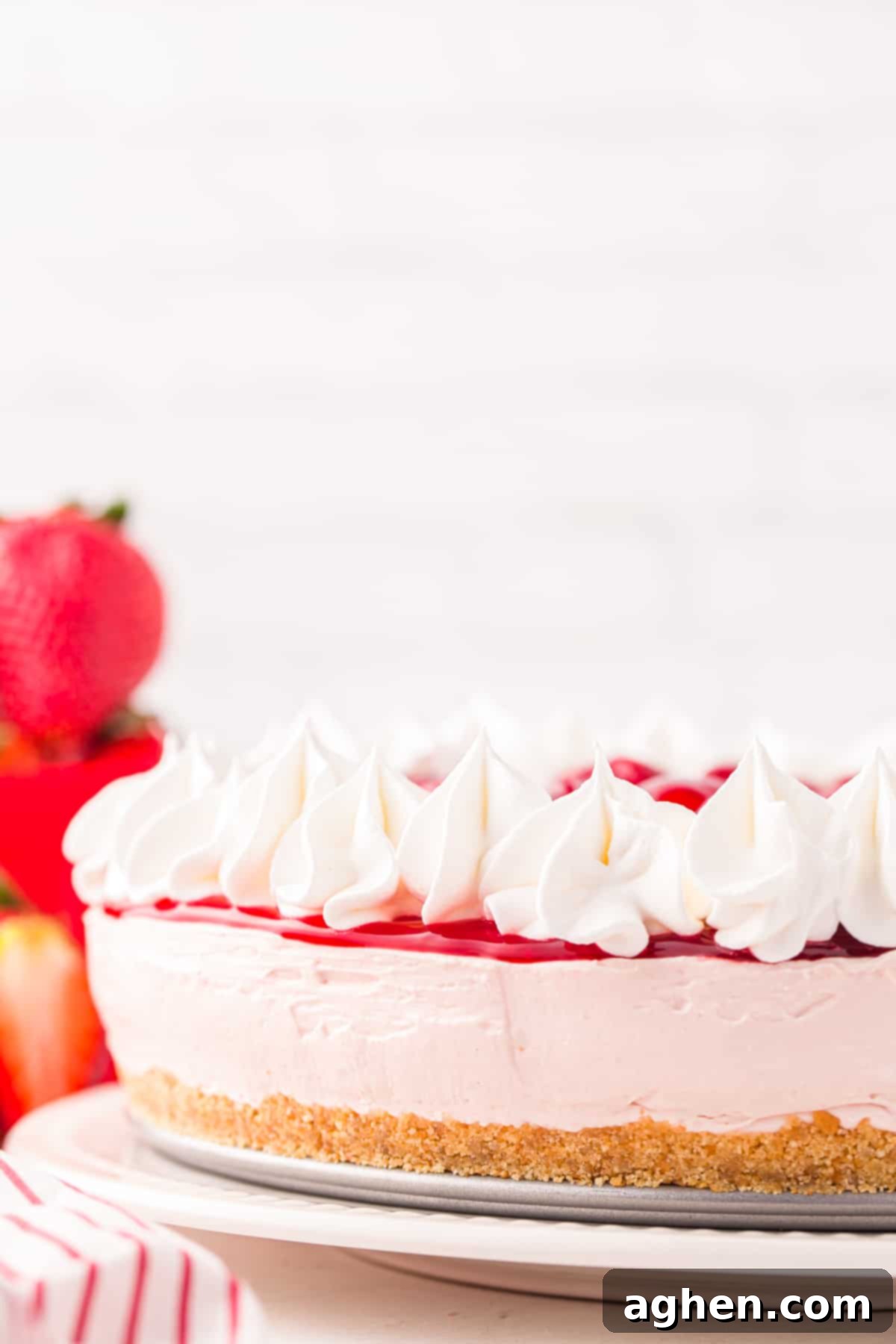 Side profile of strawberry cheesecake with buttery crust, pink cheesecake, and red pie filling and cool whip on top.