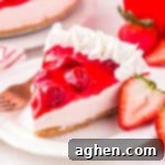 Slice of no bake strawberry cheesecake with strawberry topping and whipped cream piping on edge.