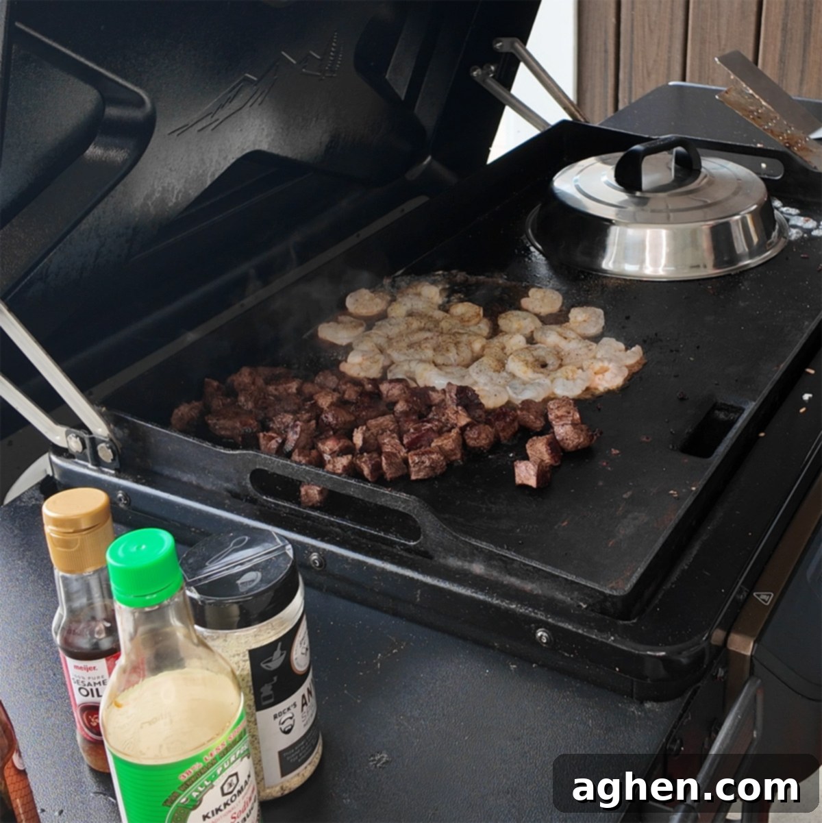 Seared steak chunks and raw shrimp cooking on the Traeger Flatrock griddle, seasoned with spices and sauces.