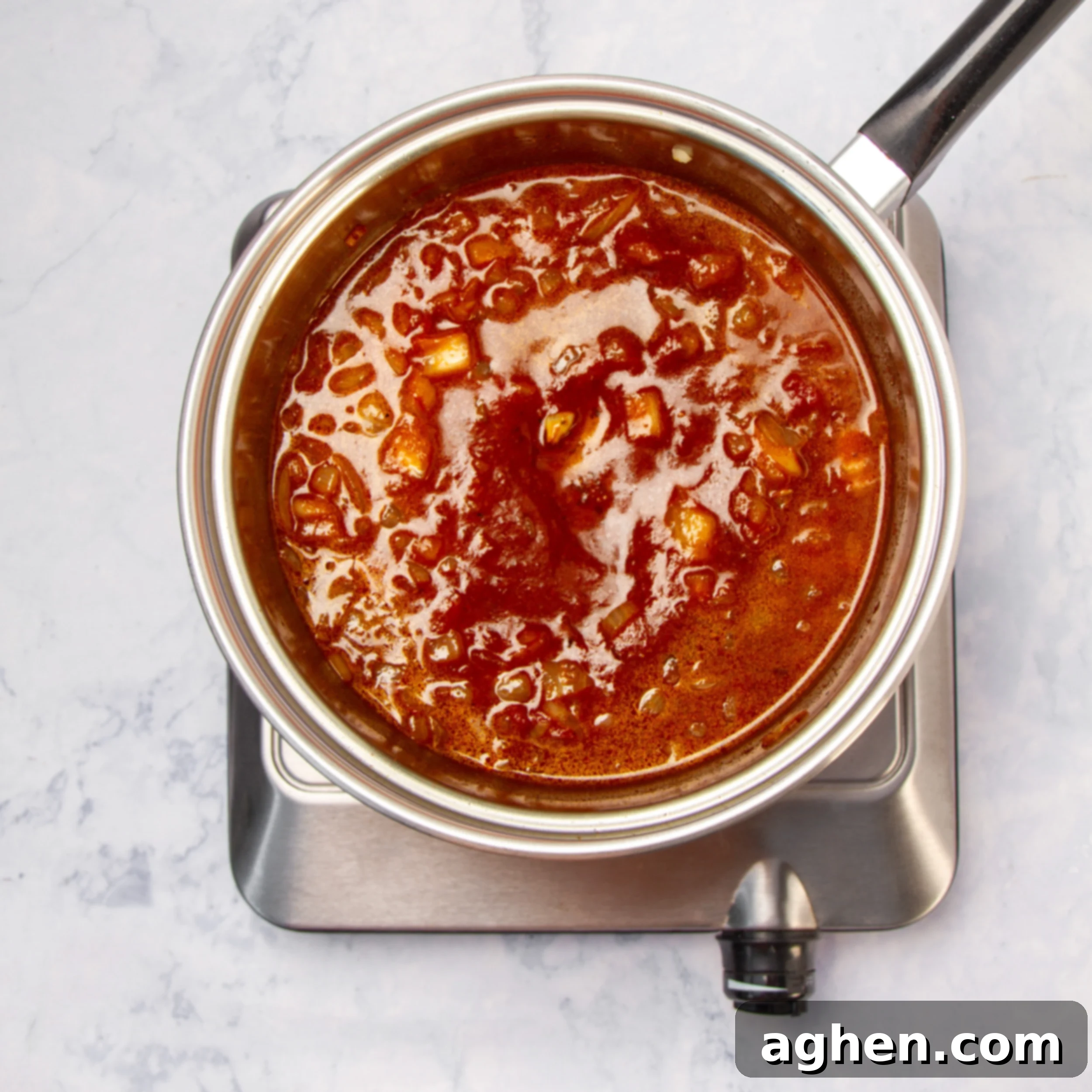 A small saucepan on the stove, containing the simmering, rich tomato-based sauce, bubbling gently.