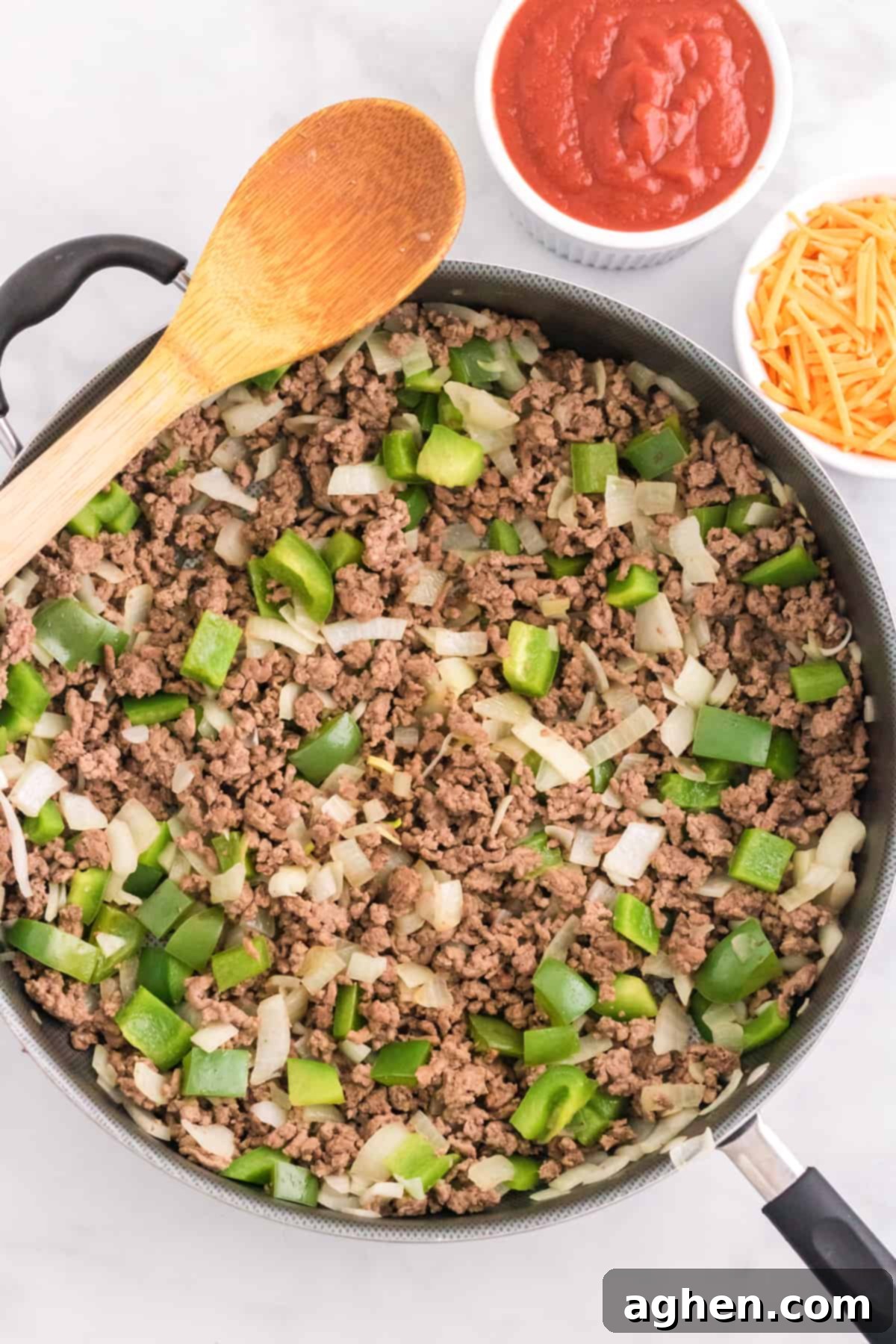 Browned ground beef in a large skillet with chopped bell peppers and onions, ready for the sauce.
