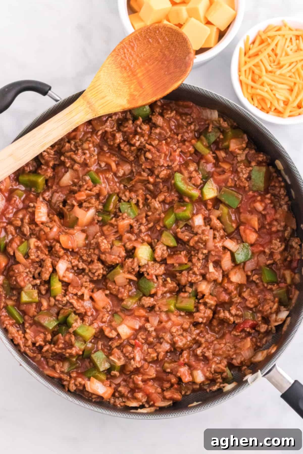 Cooked ground beef, peppers, and onions coated in Manwich sloppy joe sauce in a large skillet, simmering.