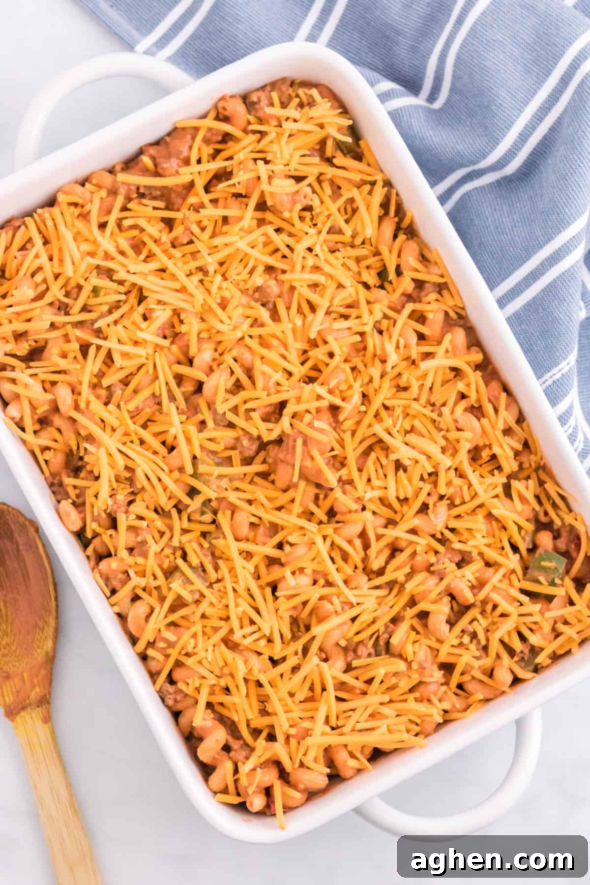 Sloppy Joe Casserole mixture covered with shredded cheese in a 9 x 13 baking dish, ready for the oven.