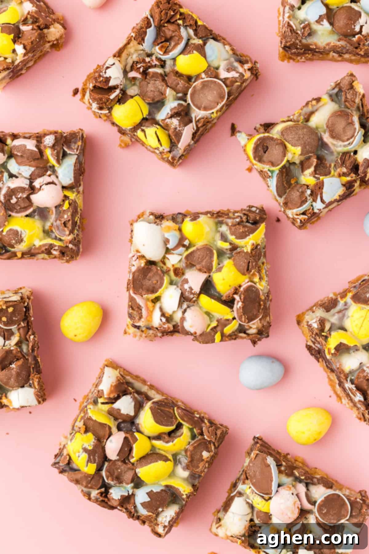 Magical Easter Cookie Bars 2 Easter magic cookie bars topped with crushed pastel mini eggs cut into squares and laid on a pink surface with additional mini eggs scattered around.