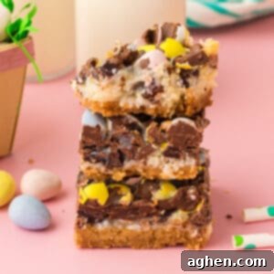 Magical Easter Cookie Bars 12 Easter dessert bars with sweetened condensed milk, chocolate chips, coconut, and chocolate eggs stacked on top of one another with top bar missing a bite.