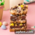 Magical Easter Cookie Bars 13 Easter dessert bars with sweetened condensed milk, chocolate chips, coconut, and chocolate eggs stacked on top of one another with top bar missing a bite.