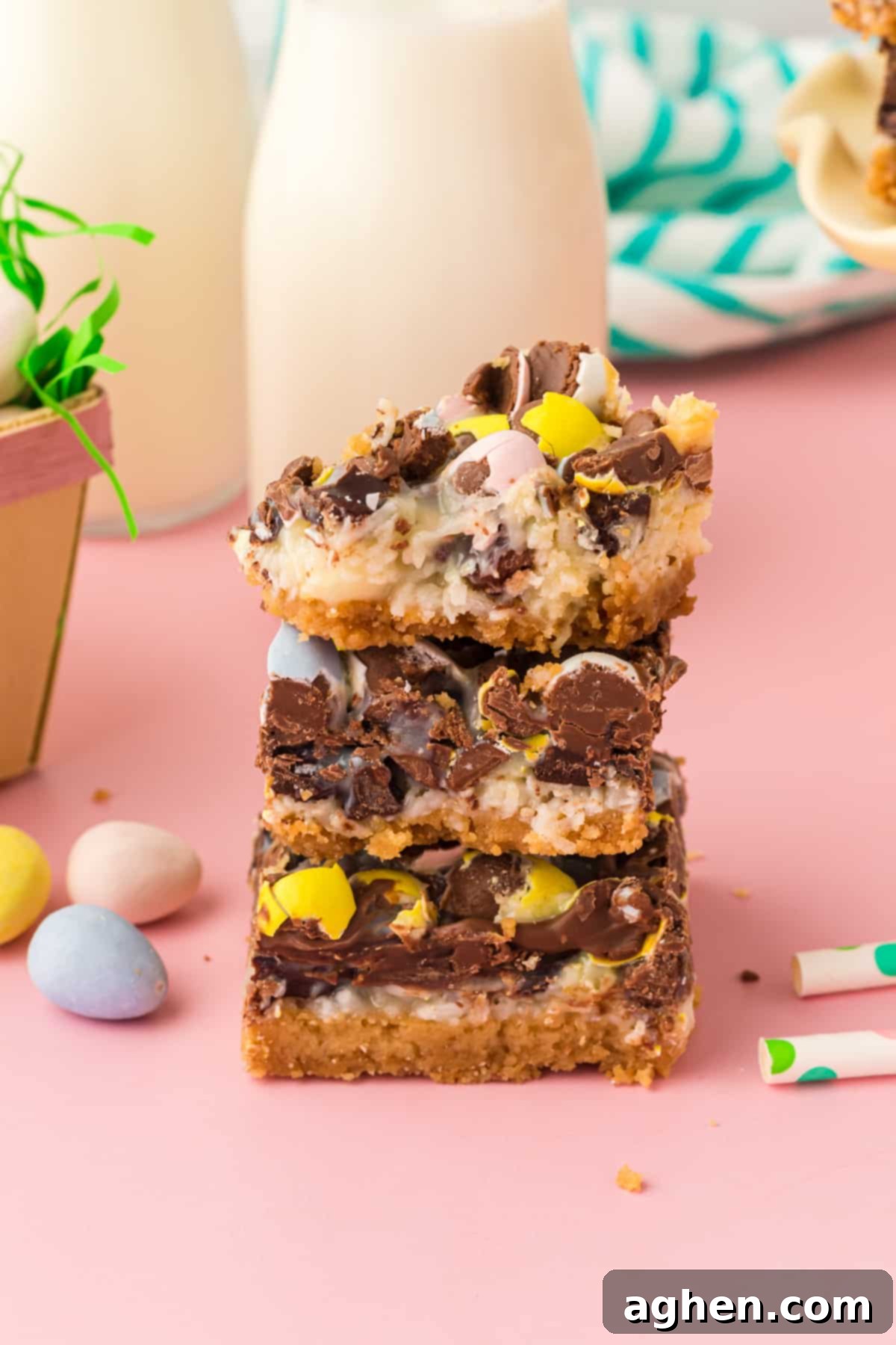 Magical Easter Cookie Bars 3 Easter dessert bars with sweetened condensed milk, chocolate chips, coconut, and chocolate eggs stacked on top of one another with top bar missing a bite.