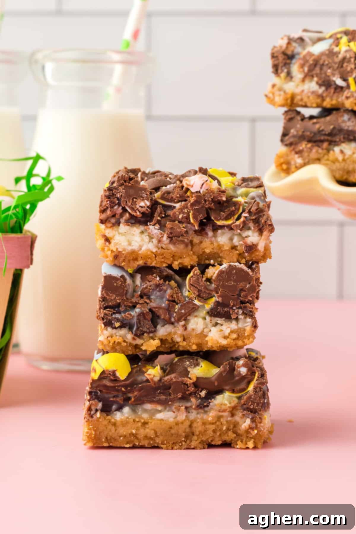 Magical Easter Cookie Bars 10 Three thick easter dessert bars stacked on top of one another with glass of milk and additional bars in the background.