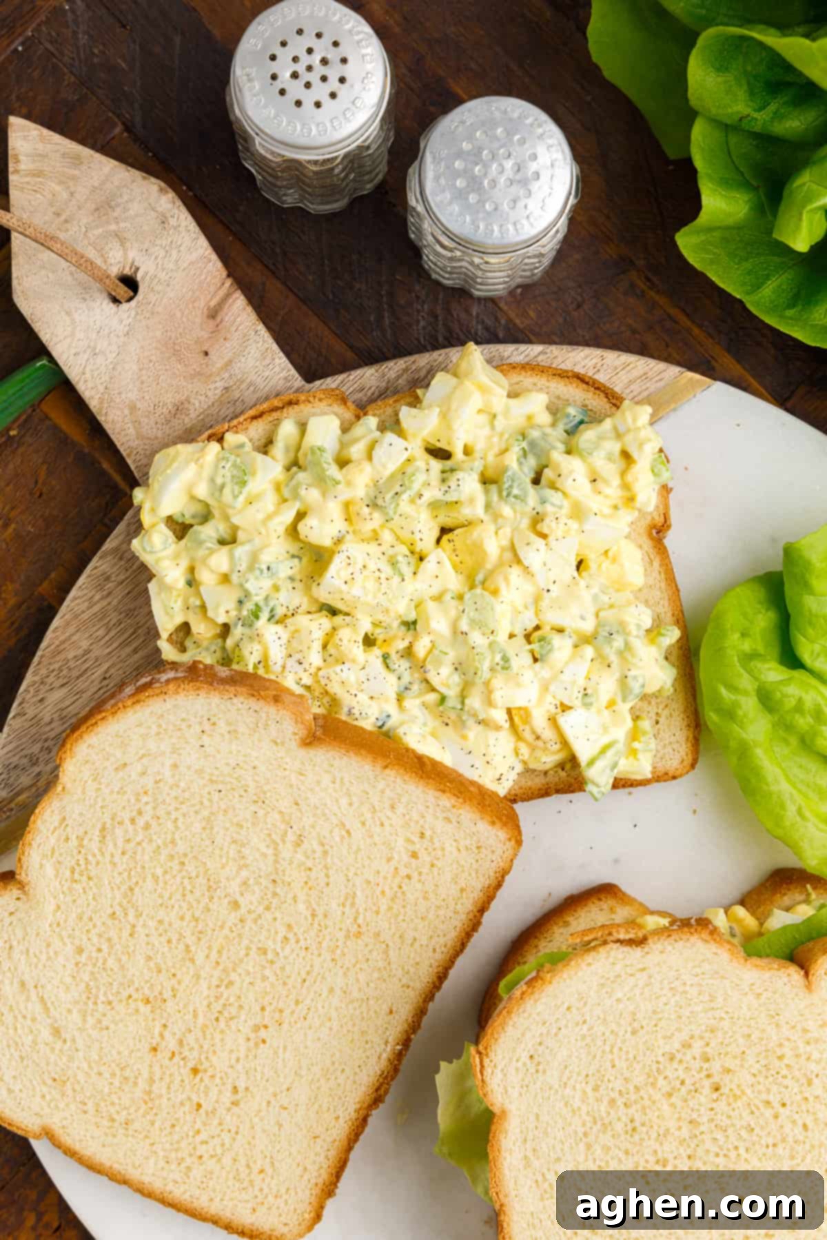 Egg salad with salt and pepper on sandwich bread with lettuce and additional slices of bread around it.