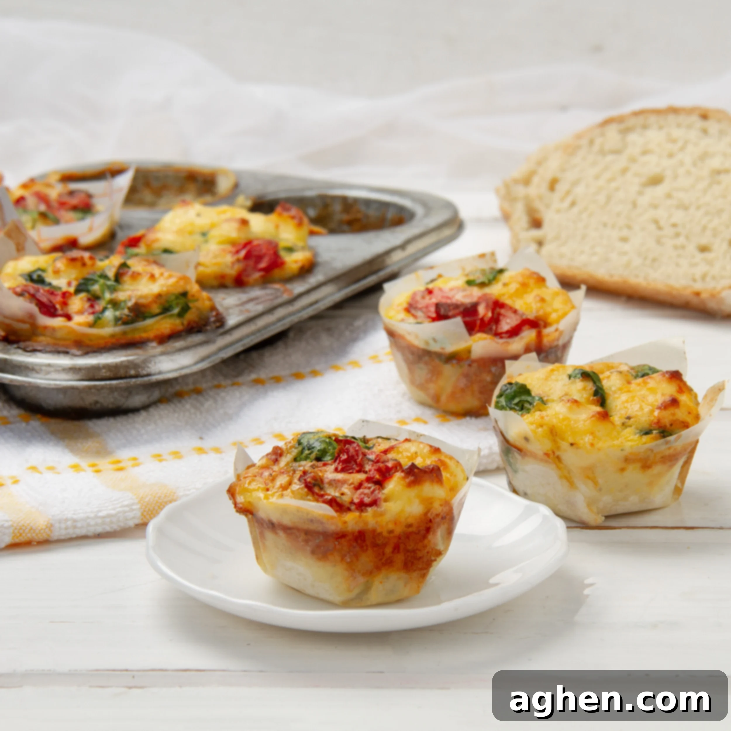 A vibrant display of freshly baked Spinach, Feta, and Sun-Dried Tomato Muffins. One muffin rests on a small white plate, two more are arranged on a rustic wooden counter, and three additional muffins are visible in the background, still nestled in a muffin tin, showcasing their golden tops and flavorful fillings.